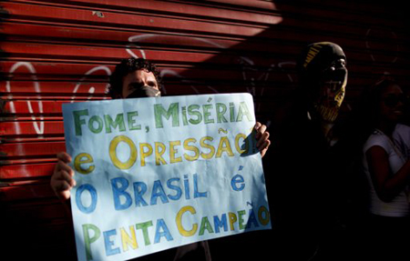 Un manifestante sostiene una pancarta en la que se lee: "hambre, miseria y opresión y Brasil cinco veces campeón" a unos metros del estadio en el que jugará Nigeria contra Uruguay en un partido de la Copa Confederaciones en Salvador, Brasil.