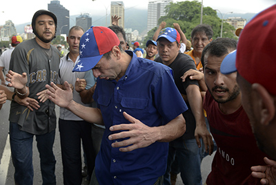 Venezuelan opposition leader and Miranda State governor Henrique Capriles (C) reacts to tear gas during a demostration in Caracas on May 11, 2016. Riot cops fired tear gas to head off a protest march Wednesday by opponents of Venezuela's President Nicolas Maduro who were demanding a referendum on removing him from office. / AFP PHOTO / FEDERICO PARRA