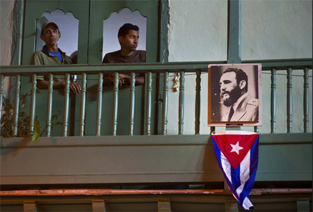 Vecinos se asoman por la ventana de su casa junto a una imagen del fallecido líder cubano Fidel Castro y una bandera cubana en La Habana, el sábado 26 de noviembre de 2016. RAMON ESPINOZA / AP( 