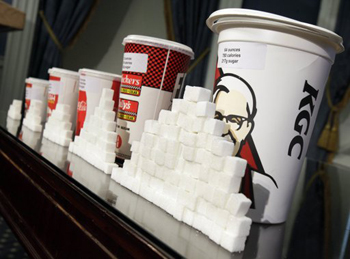 Varios vasos de refrescos son exhibidos atrás de cubitos de azúcar durante una conferencia de prensa en el ayuntamiento de la ciudad de Nueva York, el jueves 31 de mayo de 2012.