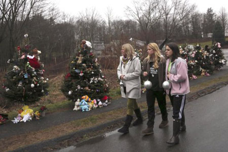 Tres mujeres llevan esferas para decorar los árboles de Navidad en uno de los monumentos improvisados para las víctimas de la matanza