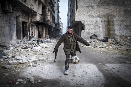 Un rebelde sirio juega arma en mano con un bal´ón de futbol, en una desolada calle de un barrio de Aleppo.