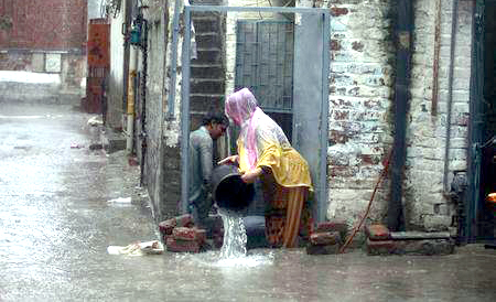 Una pareja removiendo agua de su hogar inundado por las lluvias en Lahore.