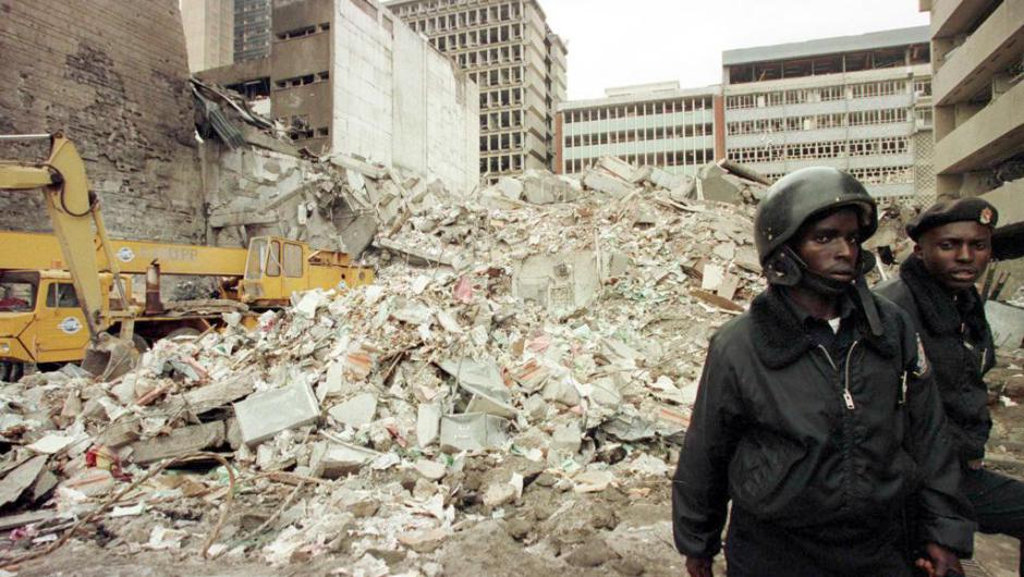 NAIROBI, KENYA:  Kenyan security guards keep watch 08 August over the scene of yesterdays bomb explosion near the US embassy in Nairobi. The latest toll from the bombing is 108 dead and more than 4,000 injured. Experts believe that there are still around 40 bodies in the rubble. No group has yet claimed responsibility. (Photo credit should read ALEXANDER JOE/AFP/Getty Images)