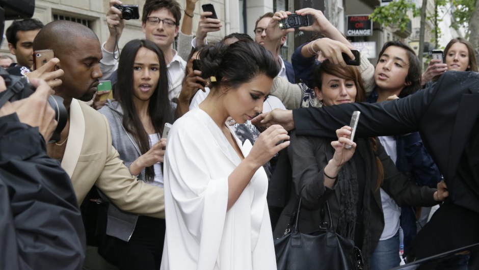 People gather around American reality TV star Kim Kardashian (C) and American singer Kanye West (L) and they leave their residence in Paris on May 23, 2014, ahead of their wedding. Kanye West and his bride-to-be Kim Kardashian lunched on May 23 at a French chateau owned by iconic designer Valentino, kicking off a marathon celebration expected to culminate in the wedding of the year. AFP PHOTO / KENZO TRIBOUILLARD        (Photo credit should read KENZO TRIBOUILLARD/AFP/Getty Images)
