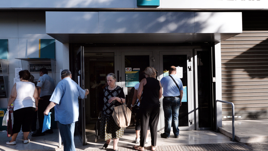 People wait outside of a national bank branch in Athens on July 20, 2015. Greek banks reopened after a three-week shutdown imposed to stop mass cash withdrawals crashing the financial system, but citizens woke up to widespread price hikes as part of a cash-for-reform deal with the country's creditors. The shutdown since June 29 is estimated to have cost the economy some 3.0 billion euros ($3.3 billion) in market shortages and export disruption. AFP PHOTO/ LOUISA GOULIAMAKI        (Photo credit should read LOUISA GOULIAMAKI/AFP/Getty Images)