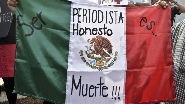 A woman holds Mexican flag with an inscription that reads "To Be a Honest Journalist is Death" during a demonstration for the murder of photojournalist Ruben Espinoza, at Angel of  Independence square in Mexico City, on August 2, 2015. Espinosa was found shot dead on August 1, 2015, in Mexico City, where he had moved two months ago from Veracruz, after reporting strong threats from the government of the state. Since 2010, 11 journalists have been killed and four others have gone missing in Veracruz. AFP PHOTO/ Yuri CORTEZ        (Photo credit should read YURI CORTEZ/AFP/Getty Images)