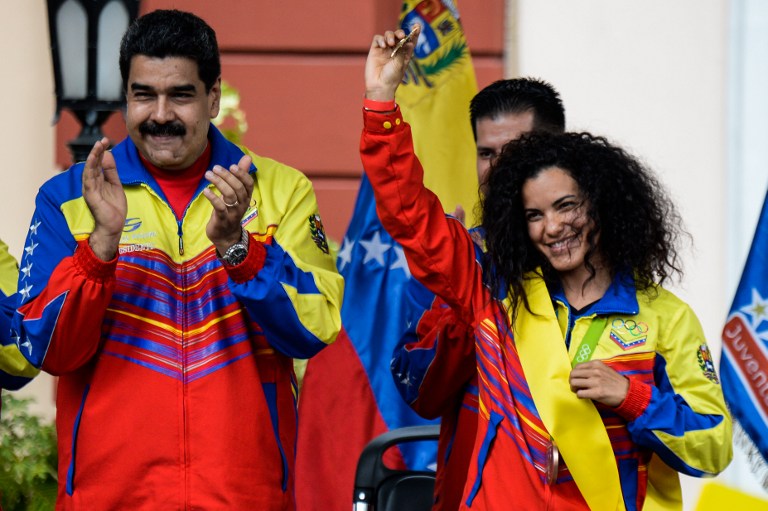 Venezuelan President Nicolas Maduro (R) applauds as Venezuelan cyclist and Bronze medallist Stefany Hernandez (L) is honored during the welcome ceremony of Venezuelan athletes who participated in the Rio 2016 Olympic Games, at the Miraflores presidential Palace in Caracas on August 22, 2016. / AFP PHOTO / FEDERICO PARRA