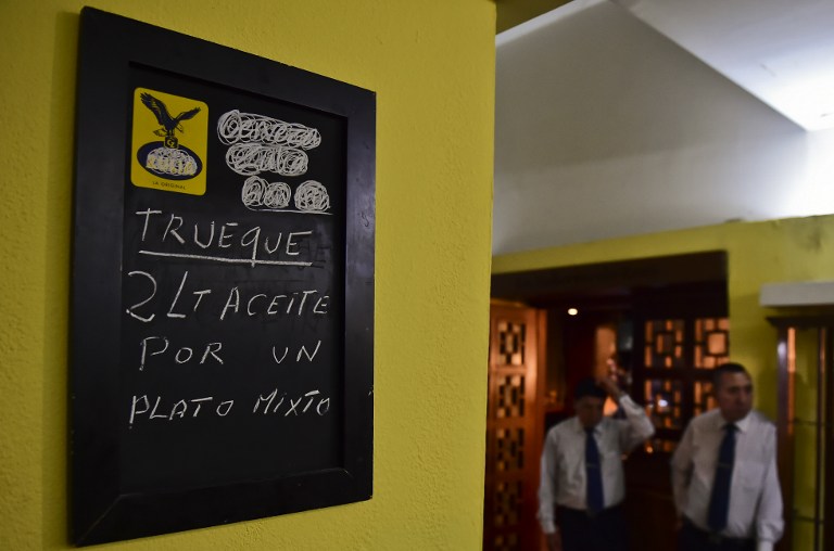 A poster offering a meal in exchange for two liters of cooking oil is seen in a restaurant in Caracas on September 13, 2016. Venezuela, a once-booming oil giant, is caught in the grip of an economic crisis marked by severe shortages of food, medicine and basic goods. / AFP PHOTO / RONALDO SCHEMIDT