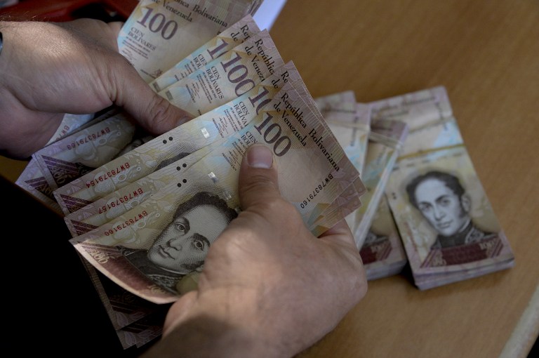 A man counts 100-bolivar-bills at an office in Caracas on December 12, 2016. Venezuelan President Nicolas Maduro on Sunday signed an emergency decree ordering the country's largest banknote, the 100 bolivar bill, taken out of circulation to thwart "mafias" he accused of hoarding cash in Colombia. / AFP PHOTO / FEDERICO PARRA