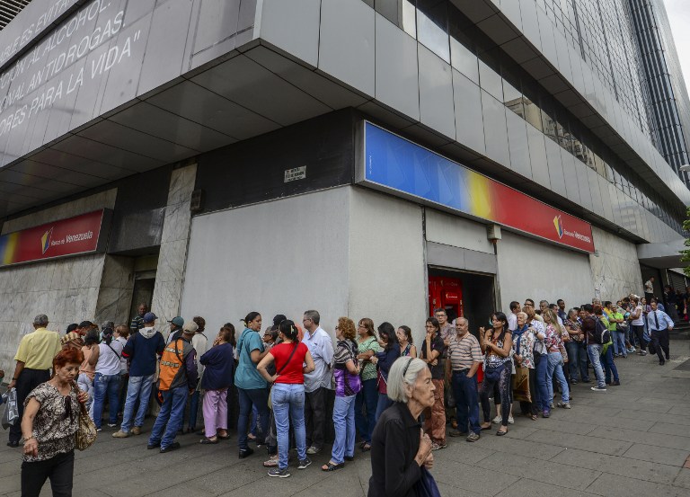 People queue outside a bank in Caracas in an attempt to deposit money, on December 13, 2016.Venezuelan President Nicolas Maduro ordered on December 12 the border with Colombia sealed for 72 hours, accusing US-backed "mafias" of conspiring to destabilize his country's economy by hoarding bank notes. The closure came a day after Maduro signed an emergency decree removing Venezuela's largest bank note, the 100 bolivar bill, from circulation because of what he called a Washington-sponsored plot against his country's troubled economy. / AFP PHOTO / JUAN BARRETO