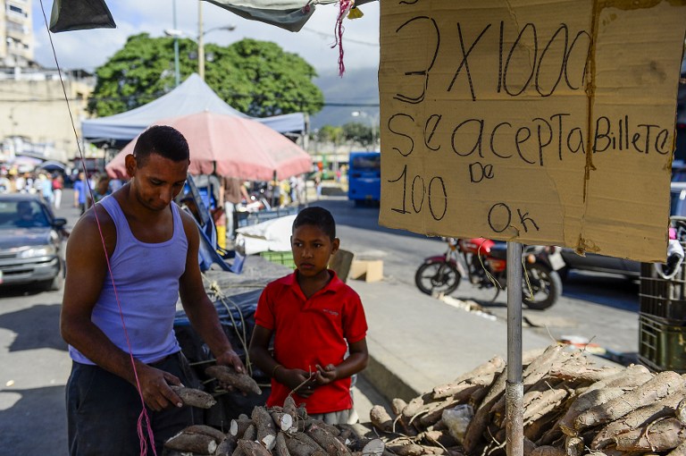 A man stands next to a sign that reads "100-Bolivar bills are accepted", at a food stall in a market at Petare shantytown in Caracas on December 19, 2016. A jetload of new currency finally arrived in Venezuela on December 18 after its delayed arrival sparked protests and looting that jolted President Nicolas Maduro's unpopular government. / AFP PHOTO / FEDERICO PARRA