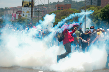 Un manifestante devuelve a la fuerza pública, envuelto en humo, la bomba lacrimógena lanzada para disolver una protesta en el este de Caracas.FEDERICO PARRA / AFP