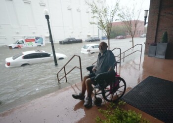 Un hombre en silla de ruedas observa desde una zona alta una calle inundada en el centro de Pensacola, Florida