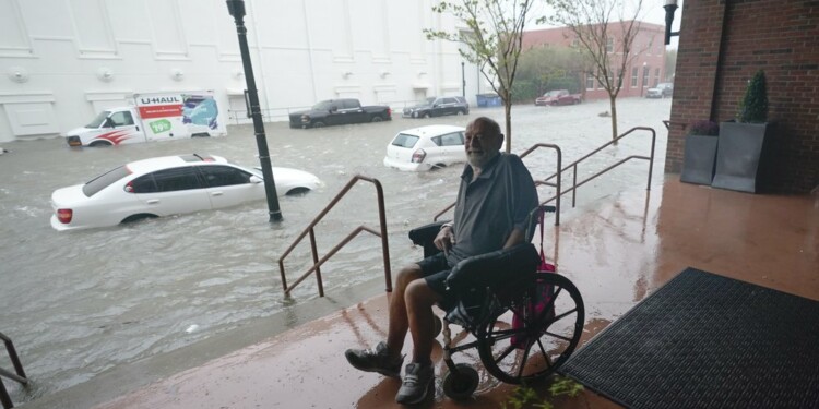 Un hombre en silla de ruedas observa desde una zona alta una calle inundada en el centro de Pensacola, Florida