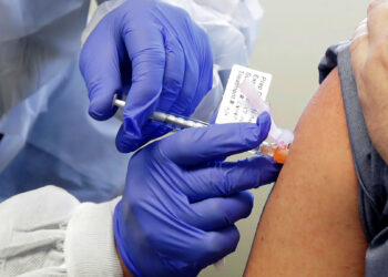 Neal Browning receives a shot in the first-stage safety study clinical trial of a potential vaccine for COVID-19, the disease caused by the new coronavirus, Monday, March 16, 2020, at the Kaiser Permanente Washington Health Research Institute in Seattle. Browning is the second patient to receive the shot in the study. (AP Photo/Ted S. Warren)