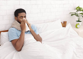 Sick black man cleaning snotty nose, lying with fever in bed, free space