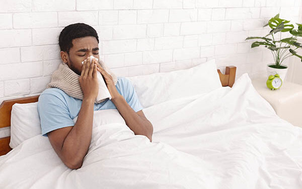 Sick black man cleaning snotty nose, lying with fever in bed, free space