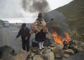 An indigenous woman stands over a barricade during the blockade of a road linking the coast and mountain areas, near Zumbahua in Ecuador on October 26, 2021 ahead of a protest against the economic policies of the government, including fuel price hikes, amid a state of emergency. - Indigenous people, workers and students will join forces to stage a protest against Ecuador's President Guillermo Lasso, who on October 18 declared a state of emergency in the country grappling with a surge in drug-related violence, and ordered the mobilization of police and military in the streets. (Photo by Rodrigo BUENDIA / AFP)