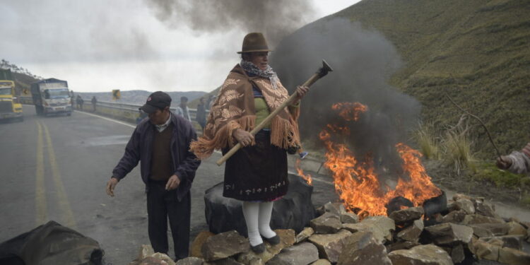 An indigenous woman stands over a barricade during the blockade of a road linking the coast and mountain areas, near Zumbahua in Ecuador on October 26, 2021 ahead of a protest against the economic policies of the government, including fuel price hikes, amid a state of emergency. - Indigenous people, workers and students will join forces to stage a protest against Ecuador's President Guillermo Lasso, who on October 18 declared a state of emergency in the country grappling with a surge in drug-related violence, and ordered the mobilization of police and military in the streets. (Photo by Rodrigo BUENDIA / AFP)