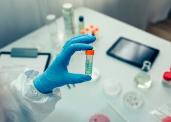 Scientist hand showing vial with vaccine in the laboratory. Selective focus on vial in foreground