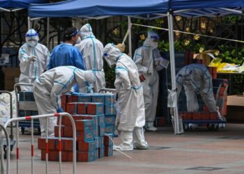 Workers wearing personal protective equipment (PPE) are seen next to food delivered by the local government for residents in a compound during a Covid-19 lockdown in the Jing'an district in Shanghai on April 10, 2022. (Photo by Hector RETAMAL / AFP) (Photo by HECTOR RETAMAL/AFP via Getty Images)