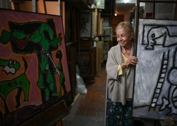 Janine Castes Vigas, the widow of the late Venezuelan artist Oswaldo Vigas (1923-2014) stands next to a painting during an interview with AFP at her husband's studio, in Caracas on January 13, 2023. - "We left it as it was": Oswaldo Vigas' atelier remains intact as it was before his death. A table served as a palette, where the renowned Venezuelan artist mixed the colors, whose work is exhibited in museums and galleries around the world. (Photo by Federico PARRA / AFP)