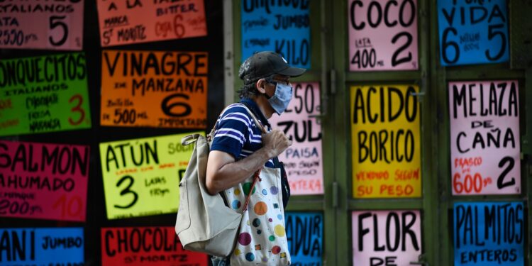 A man walks past signs displaying prices of products in US dollars outside a supermarket in Caracas on December 9, 2020. - In Venezuelan nobody wants bolivars, the weakened national currency. Everything can be payed for in dollars, which have been prohibited for 15 years, but keep gaining power in a country hit by years of recession and hyperinflation. (Photo by Federico PARRA / AFP)